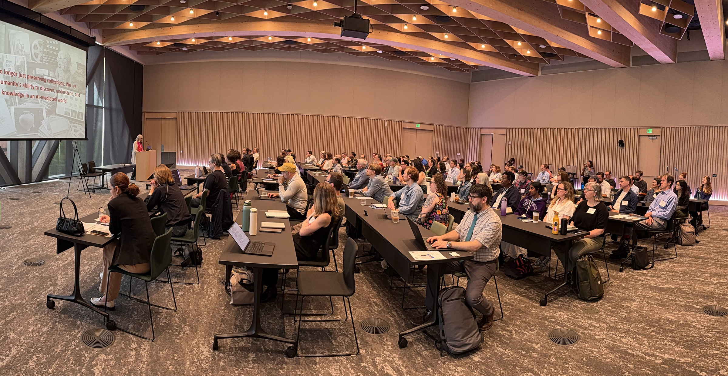 A packed room during the Can/Should AI Do That session, with a slide about preserving humanity's ability to discover, understand, and trust knowledge in an AI-mediated world